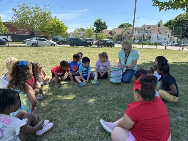 PreK watches as teacher removes butterfly from its habitat.