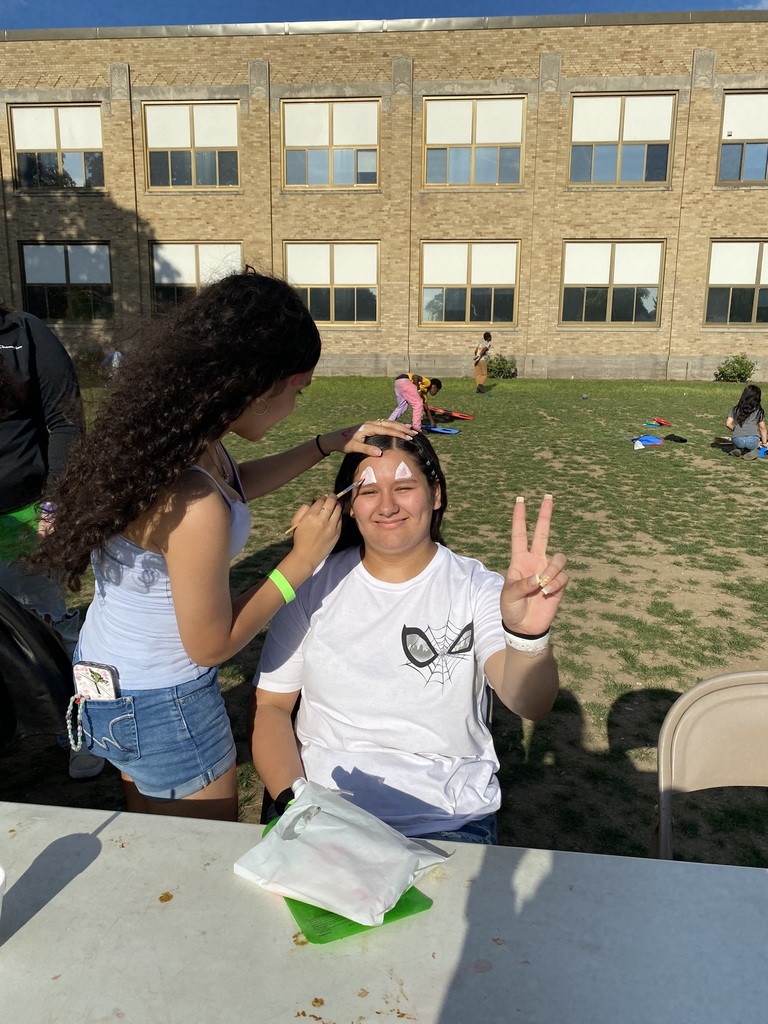 A girl getting her face painted smiles at the camera, holding up a peace sign.
