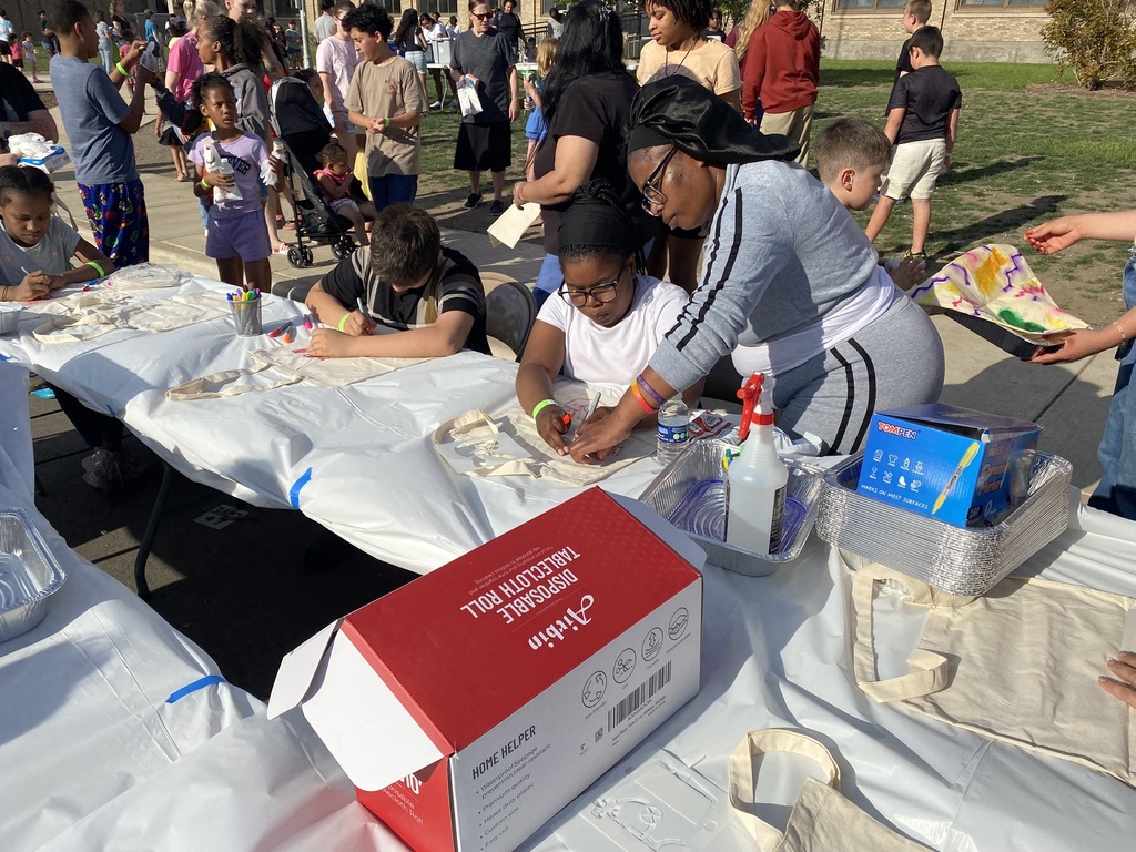 A group of students at a table draw and color on tote bags.
