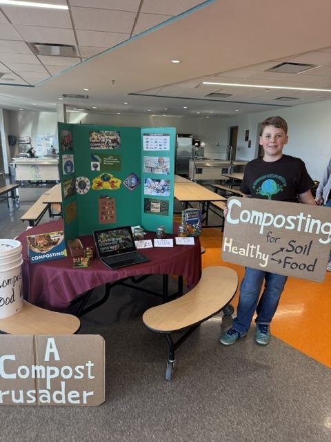 A student poses for a photo in front of their project about composting.