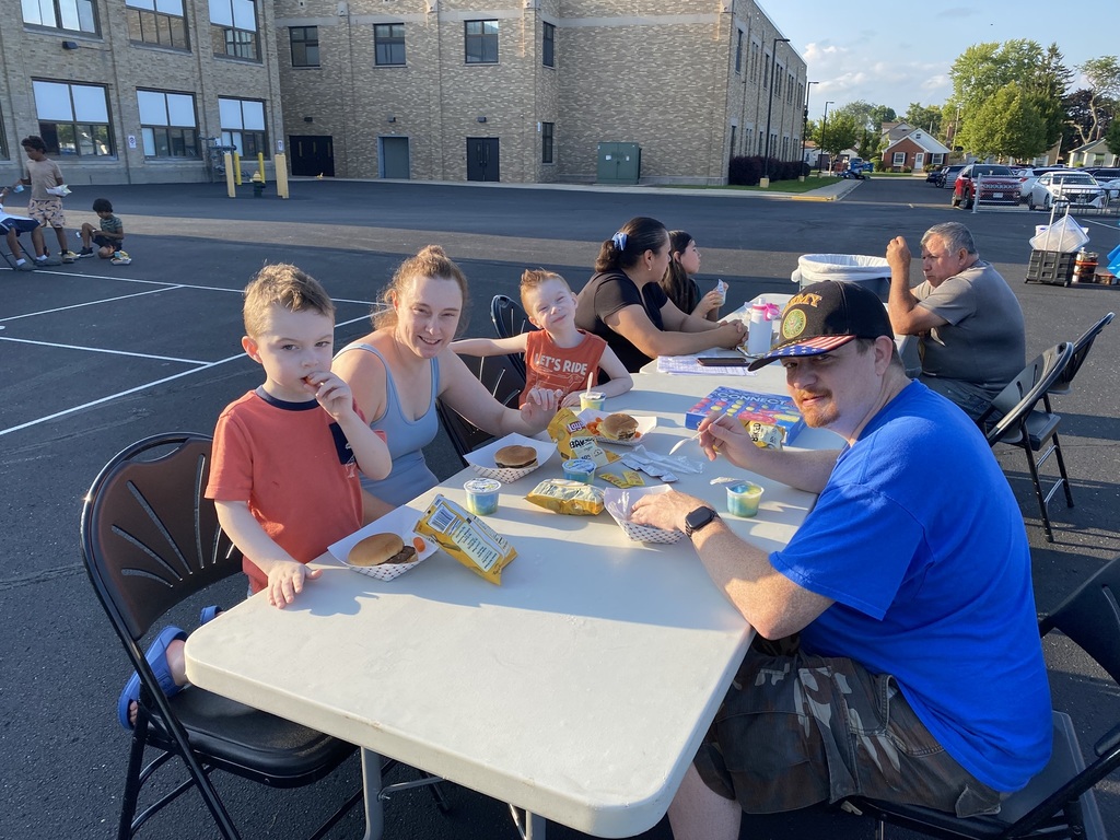 A family of 4 sitting down at a table outside and eating.