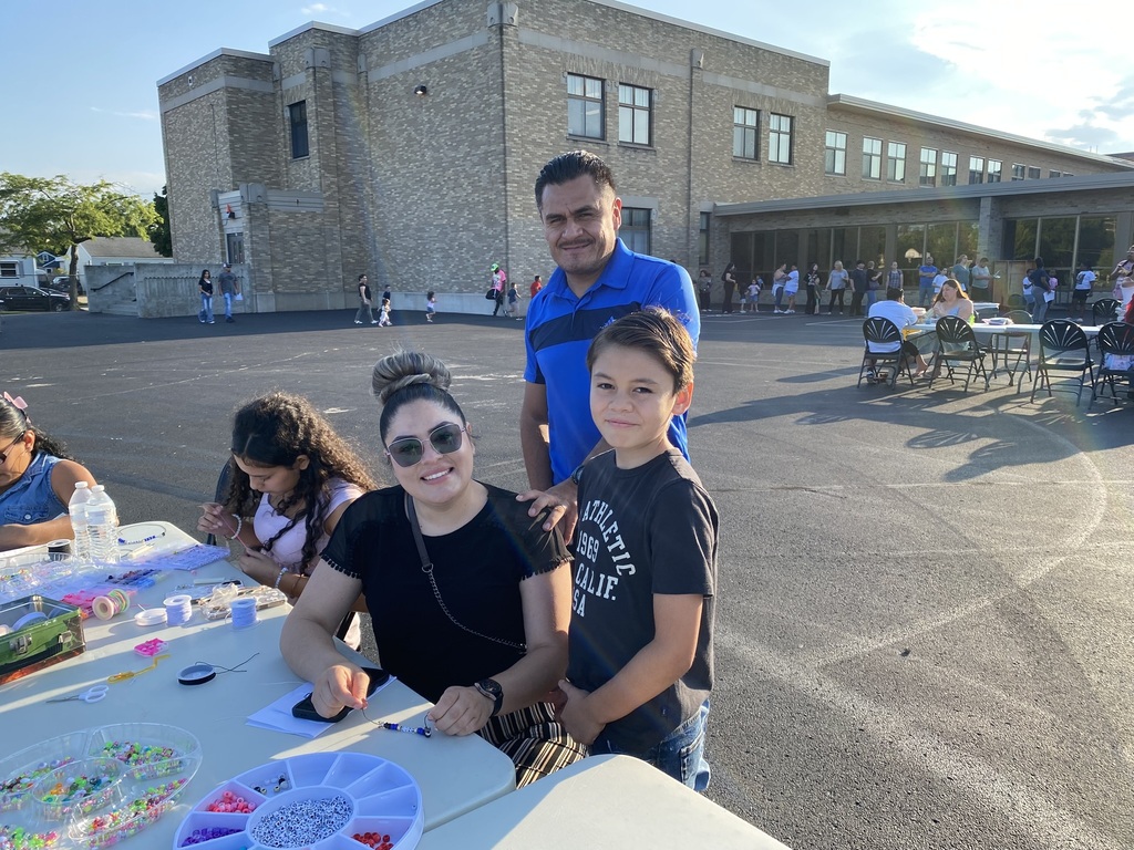 A family of 3 making bracelets at an outdoor table.