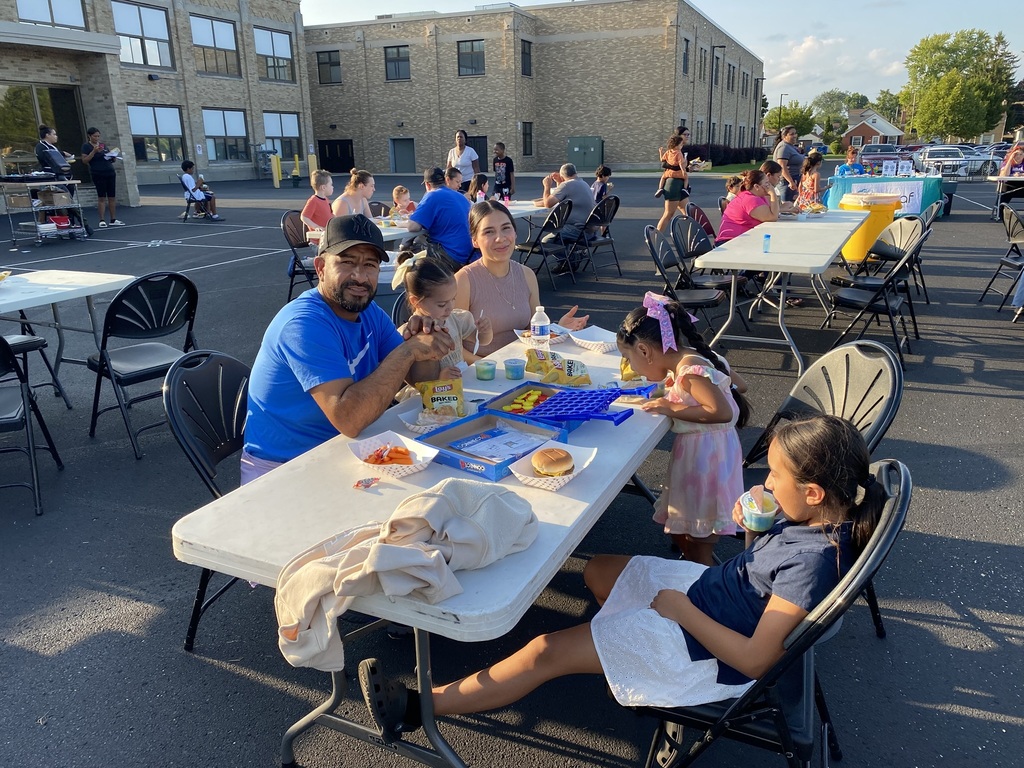 A family of 5 sitting outside at a table eating.