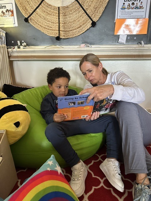 Adult reading with a little boy in the classroom library.
