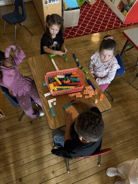 Four K4 students sitting at a table using unifix cubes to create patterns.