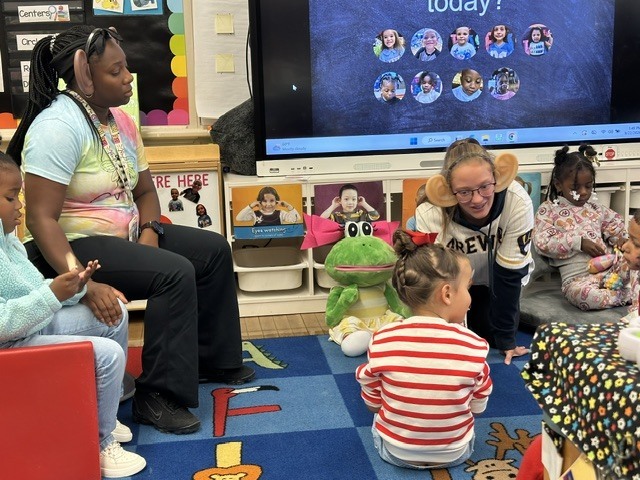 PreK teachers wear giant ears to engage students on carpet.