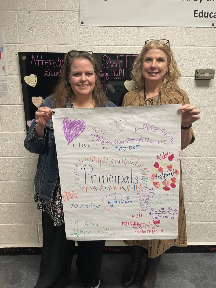 two staff members holding white poster with colored positive phrases about principals 