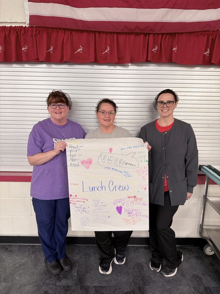 three staff members holding white poster with colored positive phrases about school lunch crew