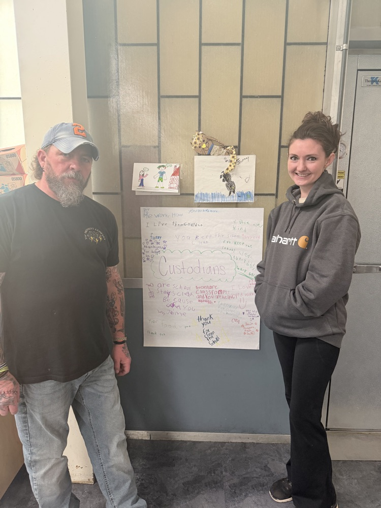 two staff members holding white poster with colored positive phrases about custodians