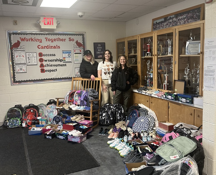 Three adults standing for a picture with shoes and backpacks on the ground