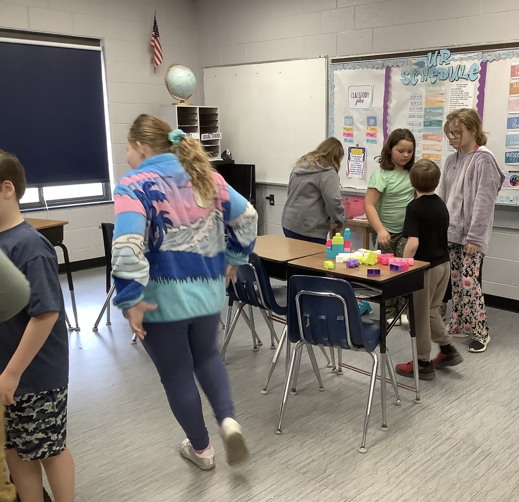 Students are standing around their desks building with blocks.