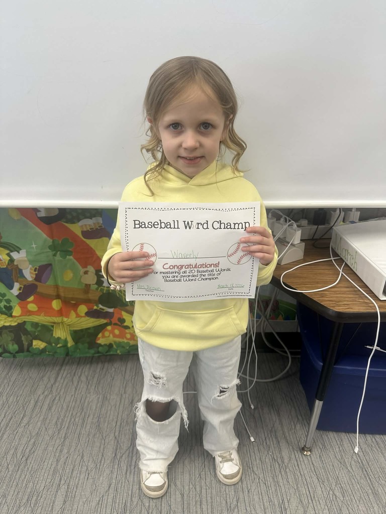 Student is holding her baseball word champ certificate and smiling.