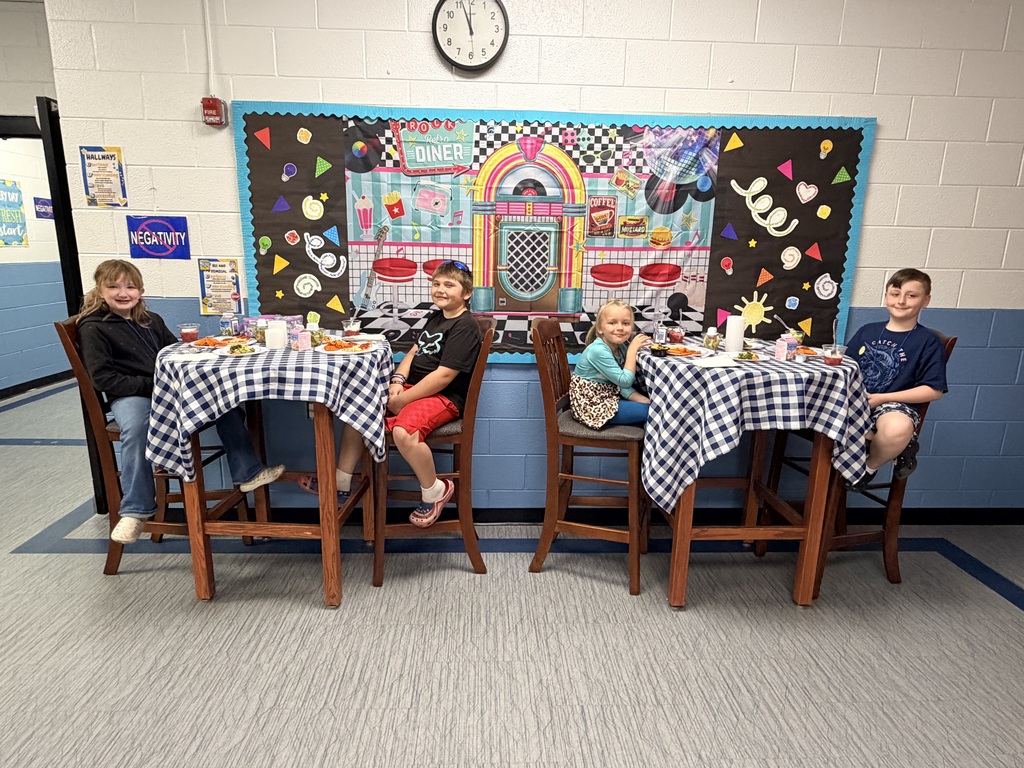 Four students are sitting at high top tables with a table cloth, candles, and fancy plates eating their lunch.