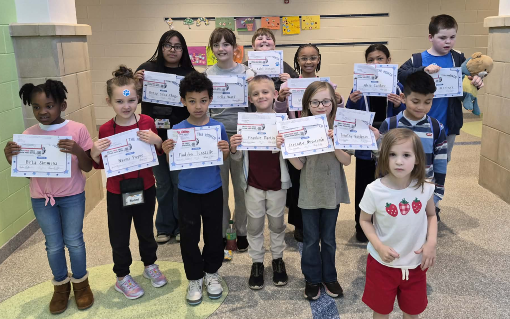 Students smiling and standing in the hallway holding their certificates