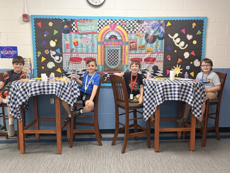Four students are sitting at high top tables eating their lunch.
