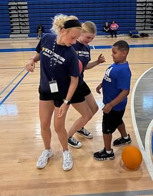 Two young summer teachers playing basketball in the gym with a student. 