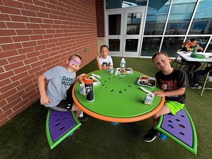 Three students eating lunch in the outdoor classroom space during Summer Camp. 