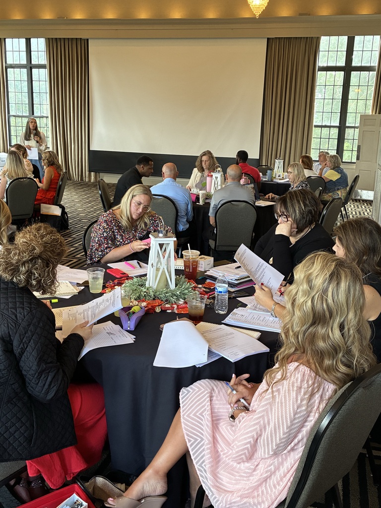 Group of women seated at a round table in a conference room, surrounded by papers, pens, and refreshments.