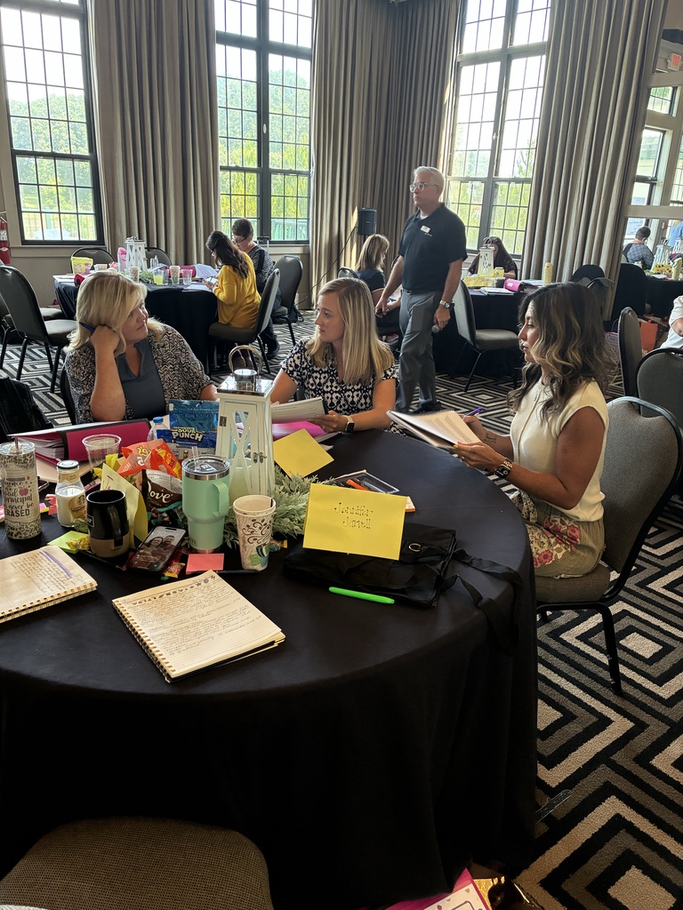 A group of people sit around a table with notebooks, yellow sticky notes, and other items.