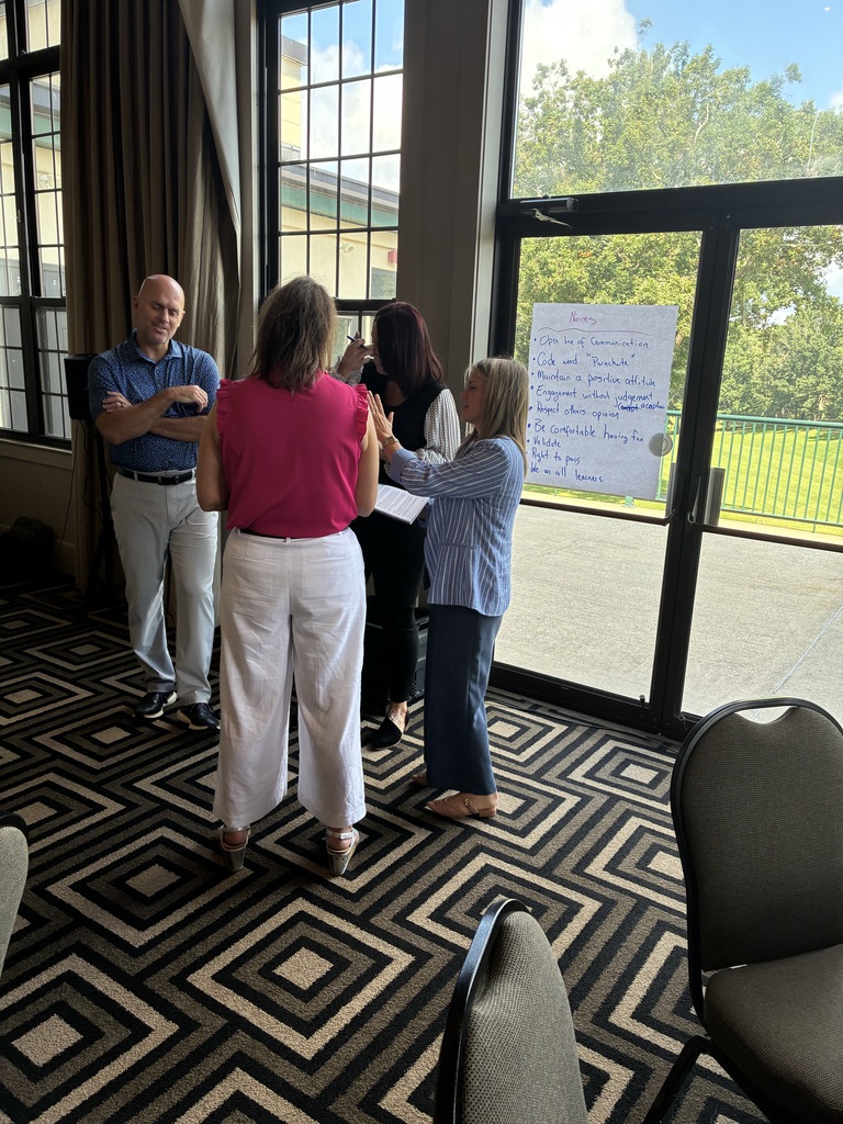 Four school administrators standing in a small group discussing a topic.  They are using a chart behind them with norms posted. 