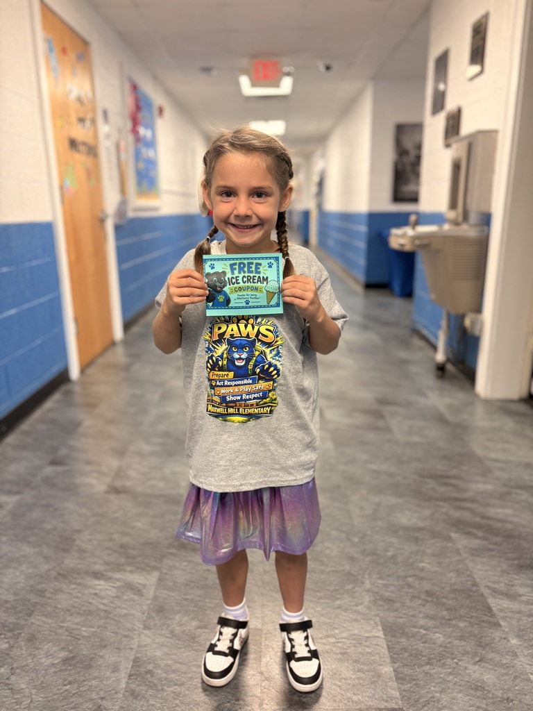 A young girl stands in a hallway, smiling, holding a green card that reads "Free Ice Cream."