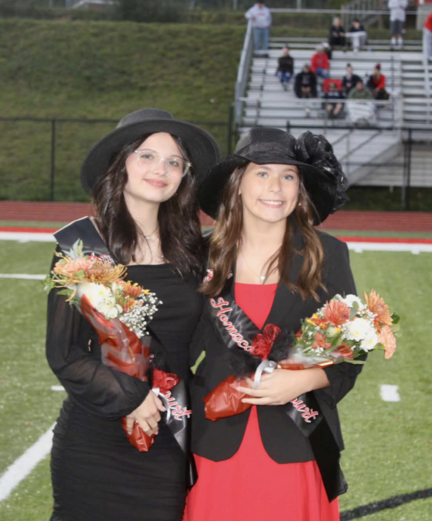 7th grade attendants for Homecoming (left)Brier Bailey and (right) Aubree Williams. They are standing on a football field with bleachers in the background 