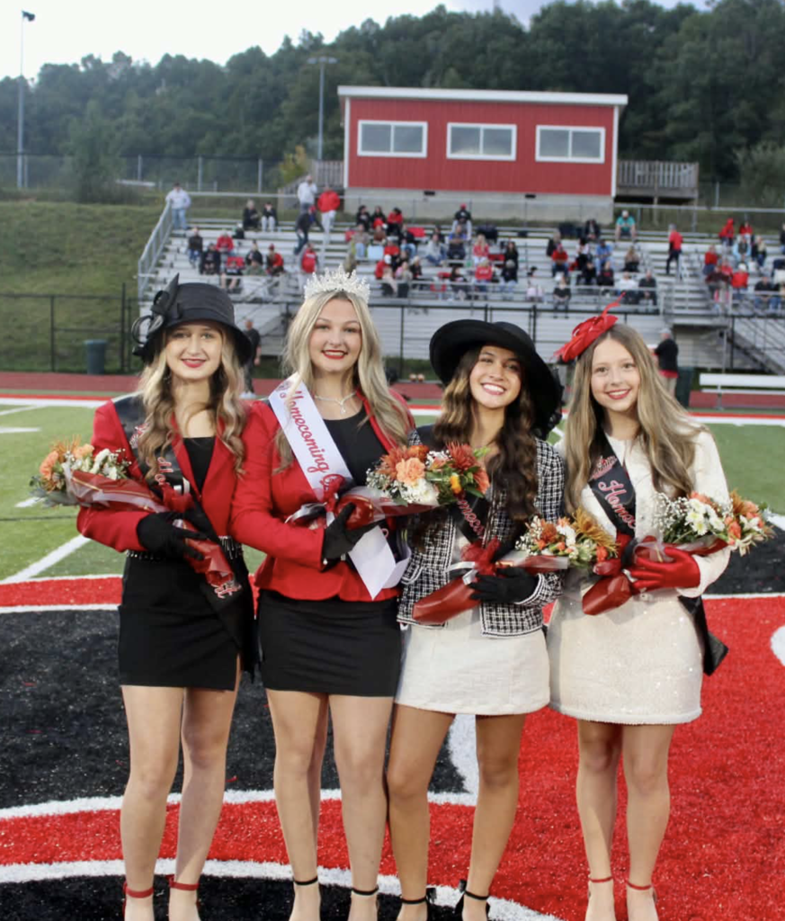 8th grade attendants, Kallie Acord, Payton Walker, Ava Yee, and Kerigan Trump.  They are standing on a football field with bleachers in the background 