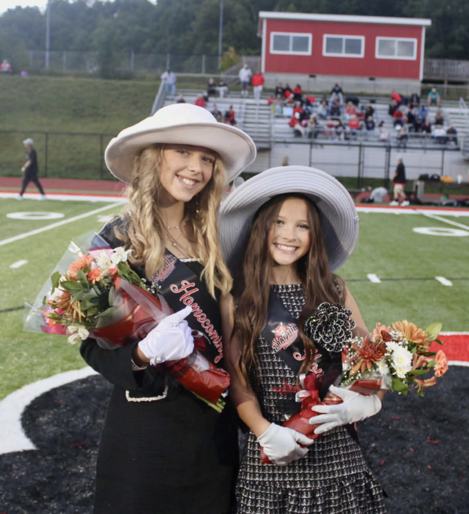 6th grade Homecoming attendants, Laken Webb (left) and Reina Yee (right).   They are standing on a football field with bleachers in the background 