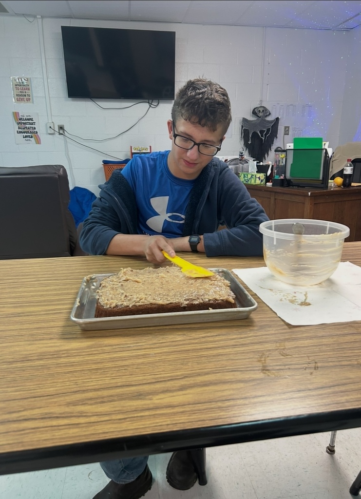 A person uses a spatula to spread frosting over a tray of brownies on a table.