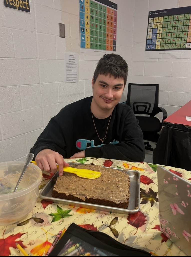 A man in a black long-sleeve shirt sitting at a table with a tray of cake in front.