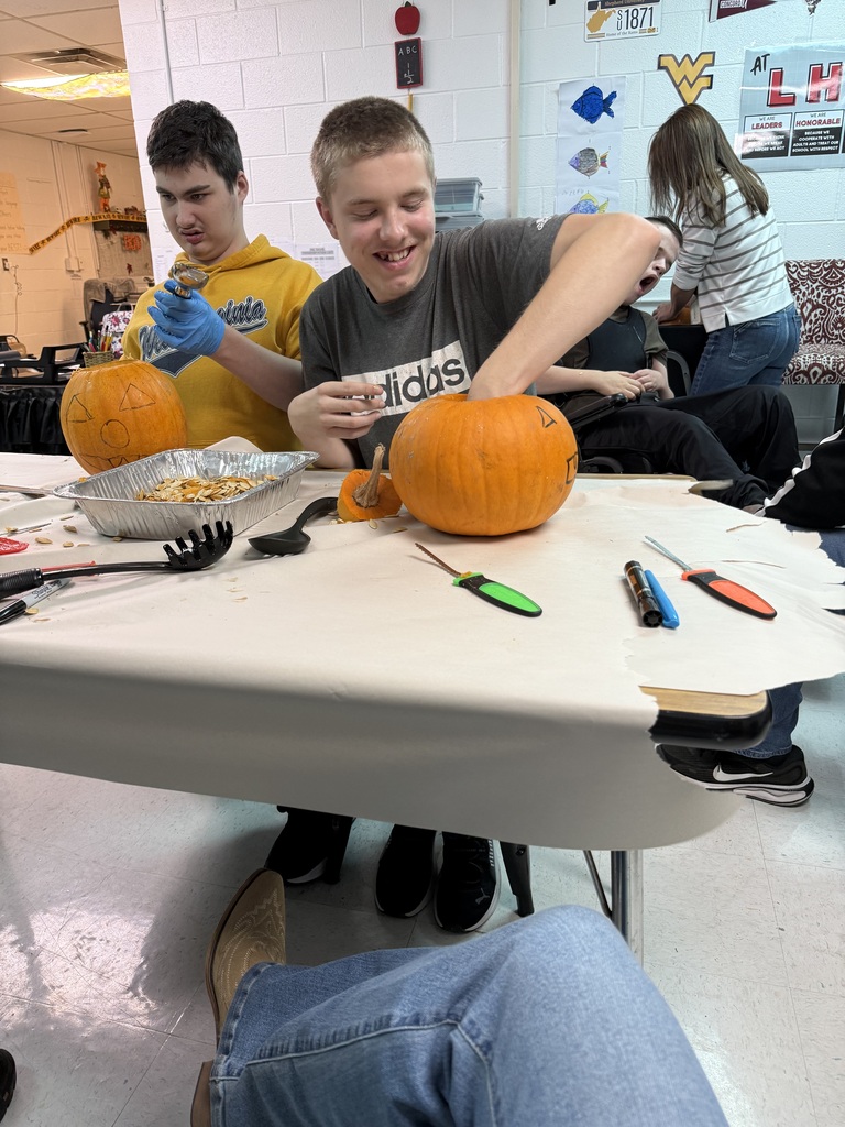 Three people carve pumpkins at a table. One person smiles and looks at the camera.