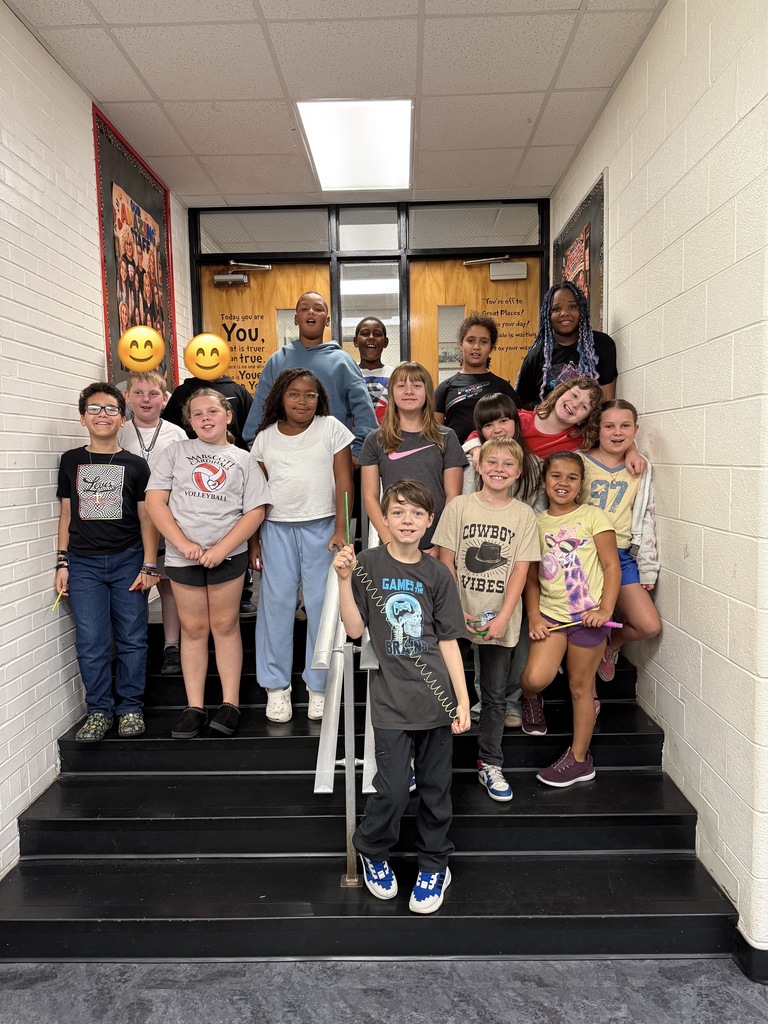 Group of students, both boys and girls, standing on stairs with two adults, one holding a cellphone.