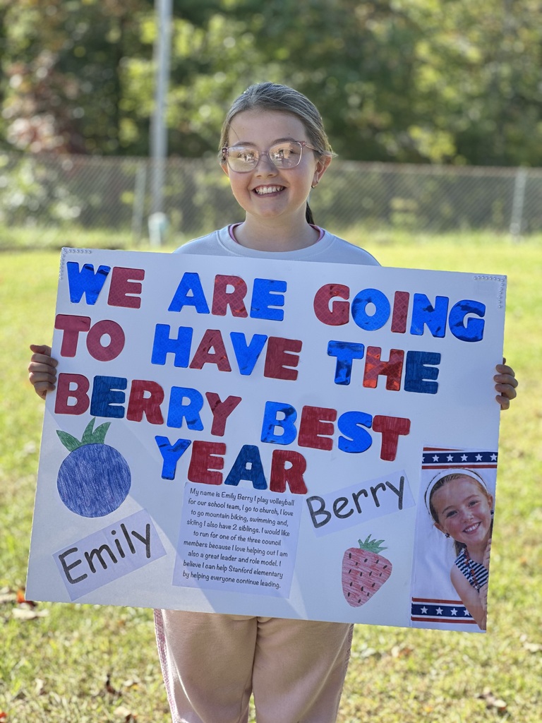 Child holds a sign saying "We are going to have the berry best year". The sign features a blueberry and strawberry.