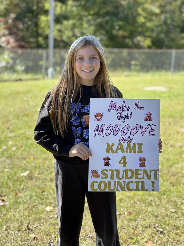 Girl stands on grass, holding a sign that reads, "Make The Right MOOOOOVE Kami Vote 4 STUDENT COUNCIL!"