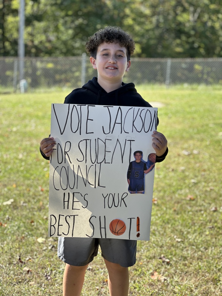 Boy holding a sign that says "Vote Jackson for Student Council. He's your best shot!" in a grassy field.