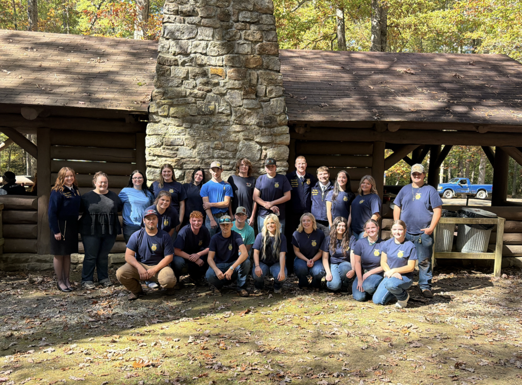 A group of people in matching uniforms, smiling, pose in front of a log cabin building.
