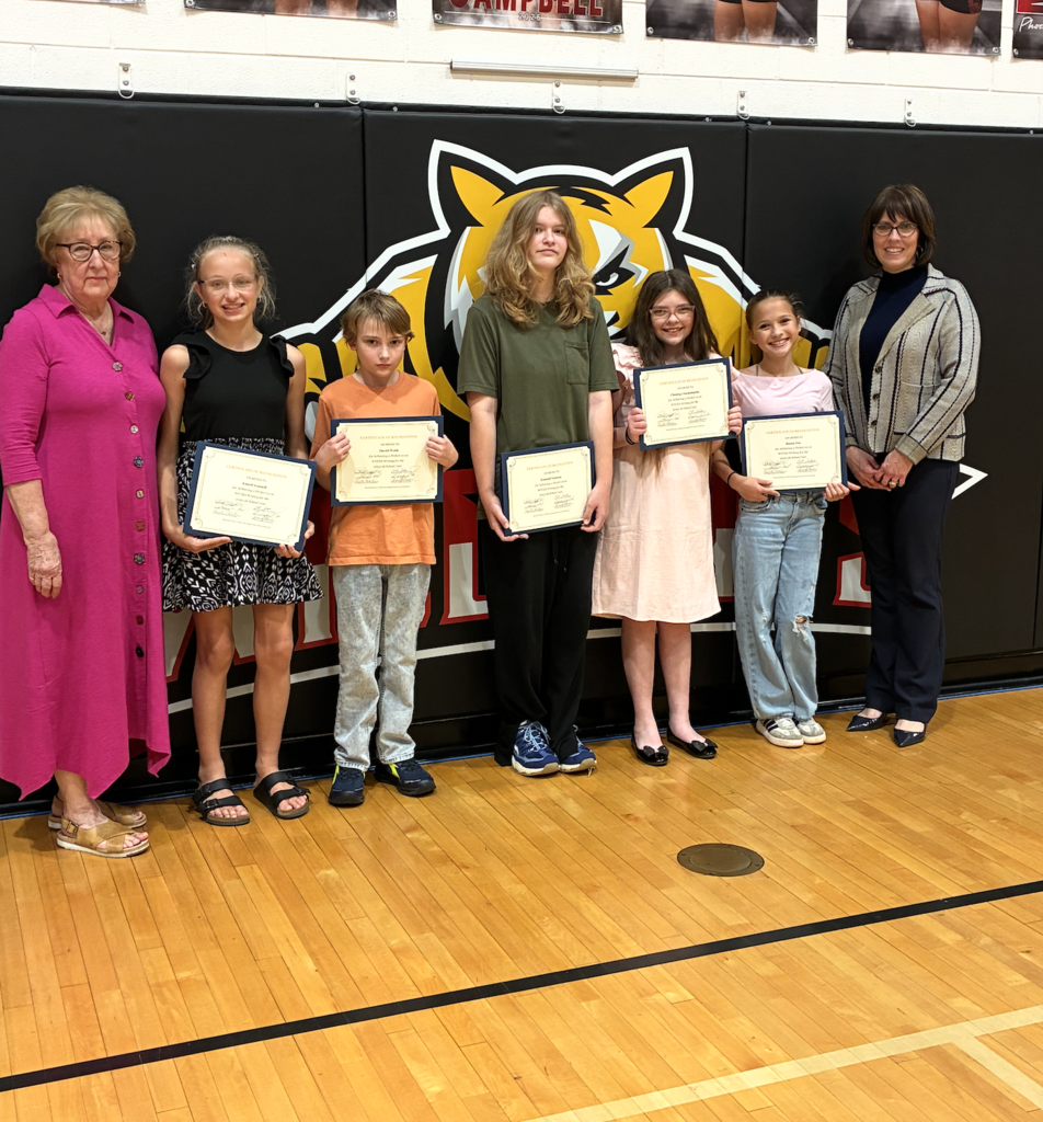Group of children and adults holding certificates. Two adults stand at the sides, four children in the middle.