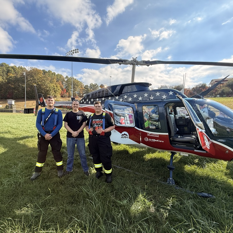 three men standing in front of a medical helicopter in a field 