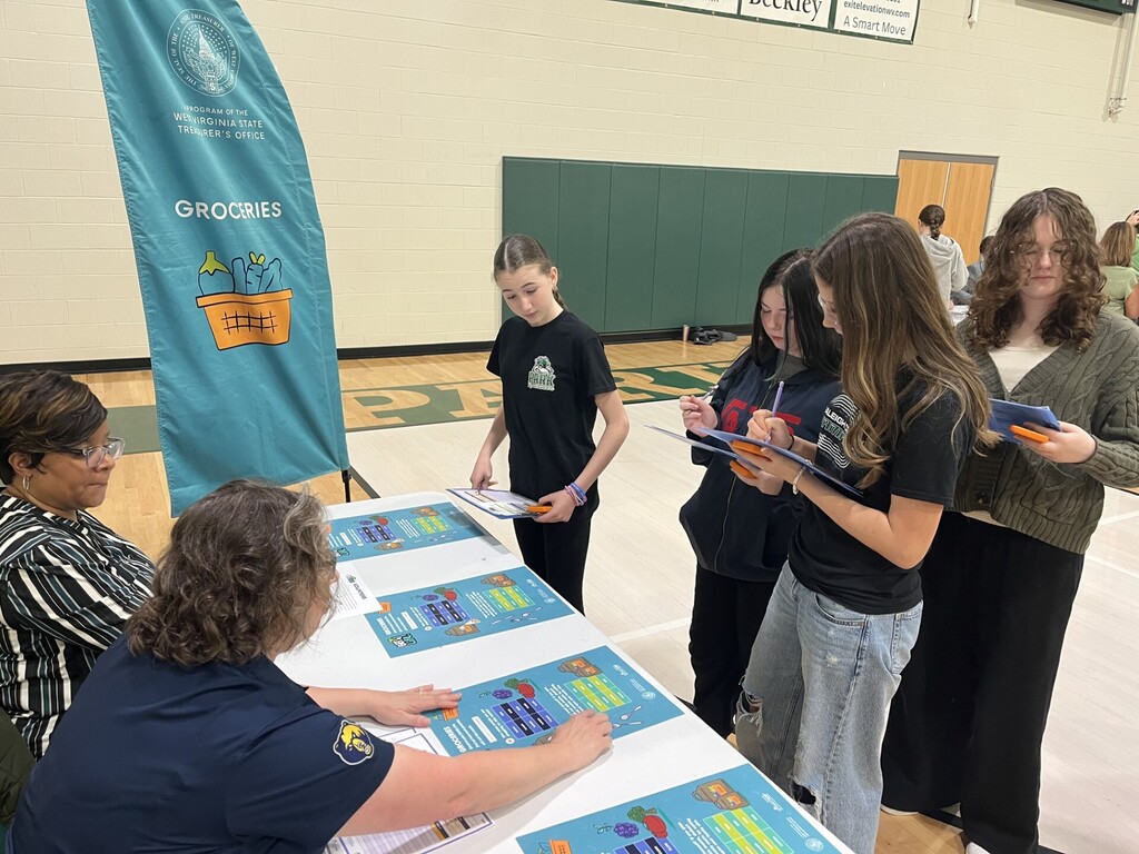 Group of people at a table with informational brochures, a woman seated in front and another holding a flyer.