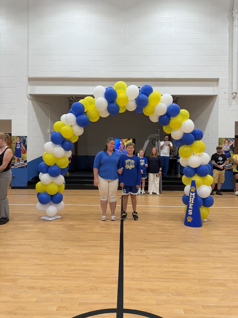 Three people under a colorful arch of balloons in a gymnasium. One wears a sports uniform.