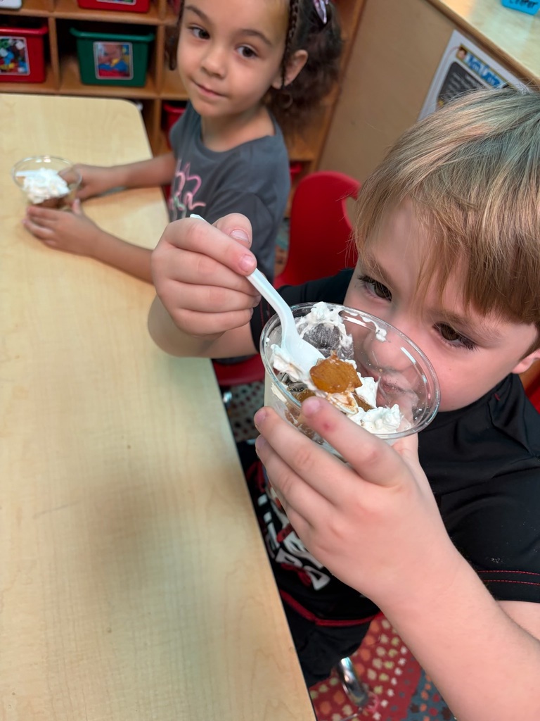 Two children at a table. A boy holds a bowl with a spoon and a girl holds a cup.