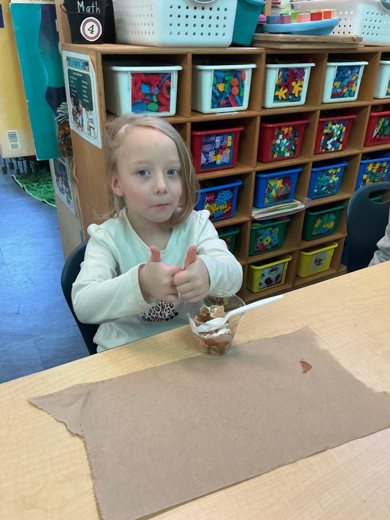 A child sits at a table with a bowl of food. Behind the child is a shelf with many storage boxes.