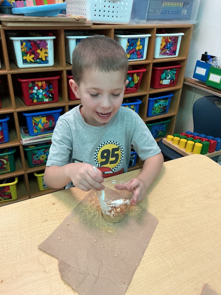 A child in a blue shirt uses a spoon to mix food in a clear container.