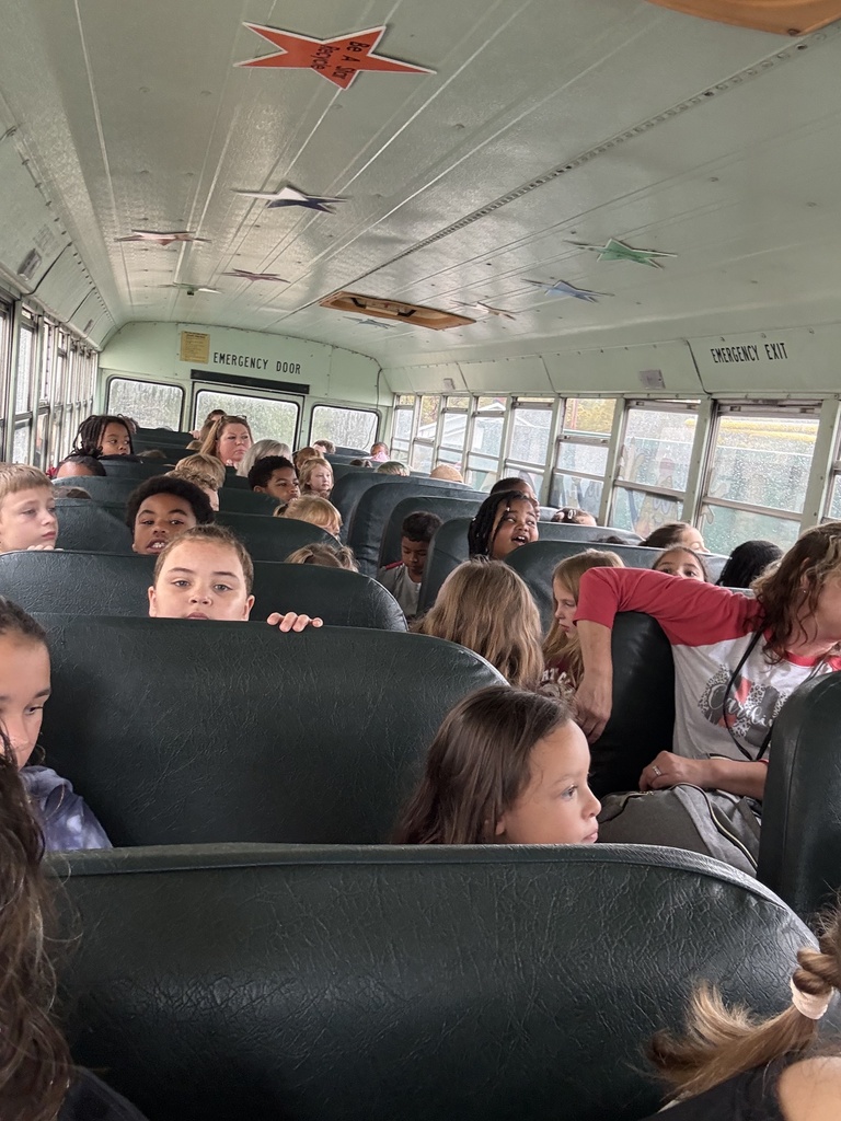 A bus with children sitting in rows of seats. One child is looking up at the ceiling.