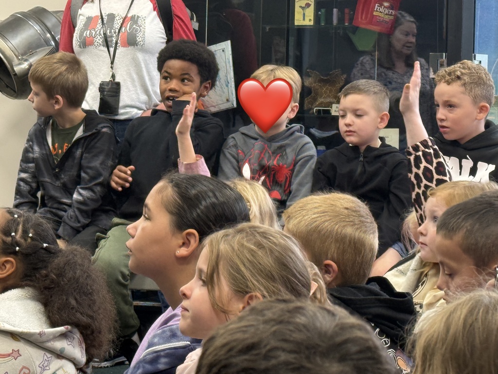 Several children seated and standing, one holding a red heart sticker over mouth, in a room