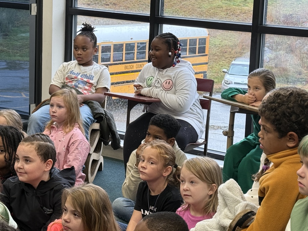 A classroom with glass windows showing a school bus outside, where children are seated listening