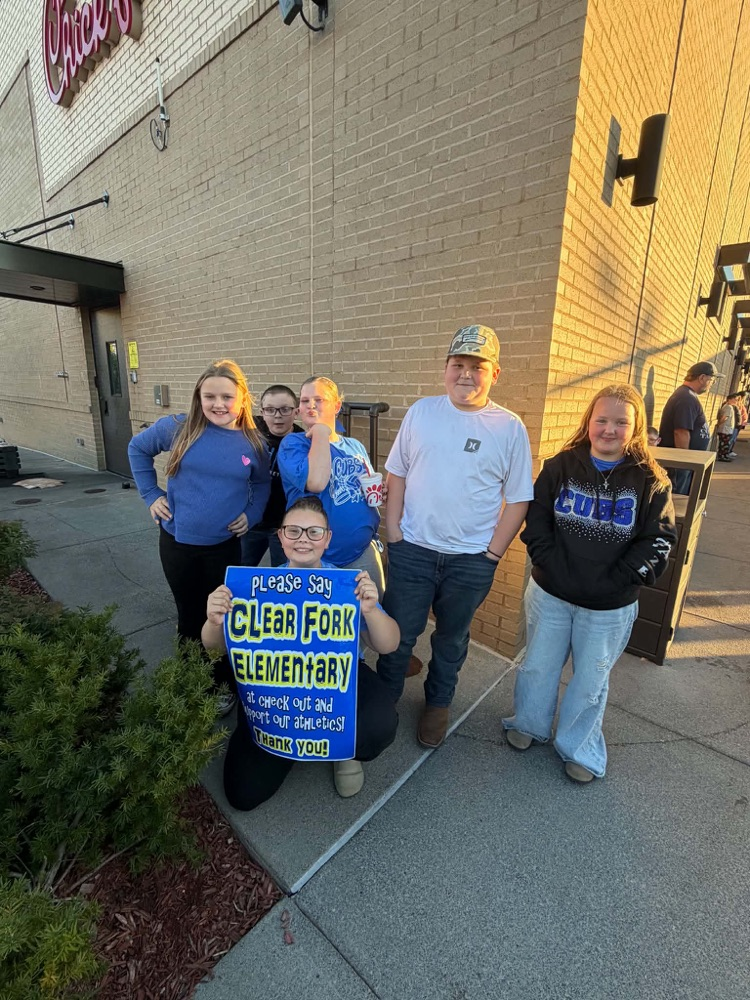 Six people stand together outside a building. One person holds a blue sign. The sign reads, "Clear Fork Elementary".