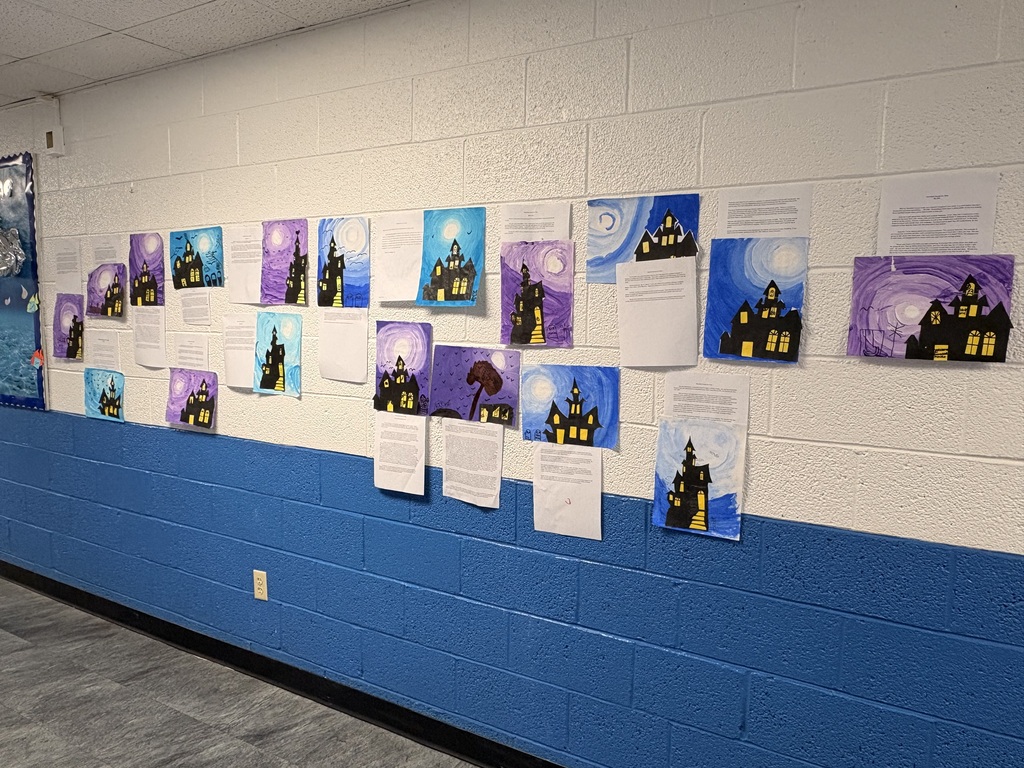 Artwork displayed along a blue wall. Artwork includes illustrations of houses and trees. Papers attached to the wall.