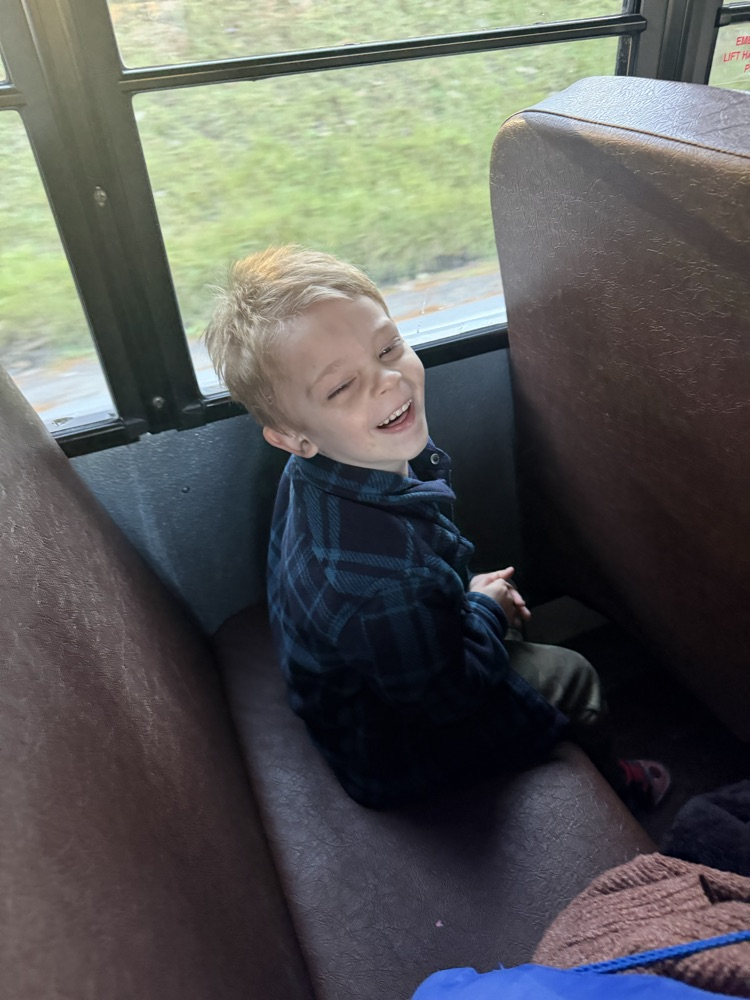 Young boy wearing a blue and black plaid shirt sitting on a school bus seat.