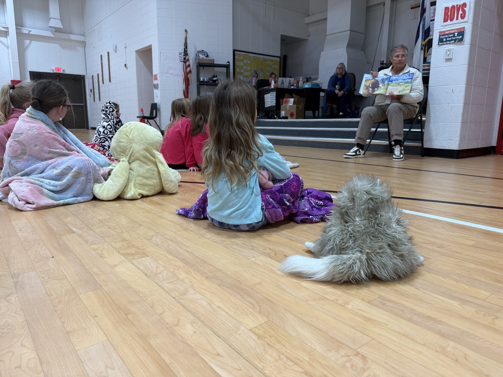 A person reads a book to children sitting on the floor in a gym.